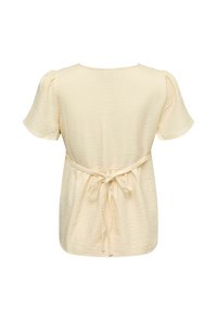 Blouse crème à manches courtes avec tissu texturé et un fin nœud de ceinture à l'arrière, vue de dos sur fond blanc.