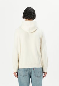 Crème hoodie met een relaxte pasvorm, geribde mouwen en zoom. Gepaard met lichtblauwe denim jeans met achterzakken.