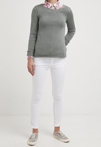 Grå stickad tröja med en blommig skjorta under, kombinerad med vita tajta jeans och mönstrade sneakers.