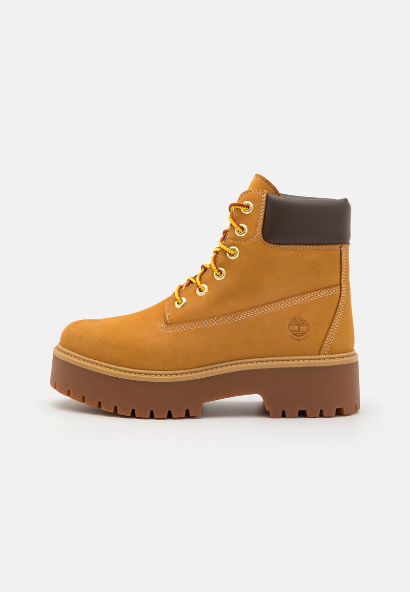 Gelbe LederStiefelette mit braunem gepolstertem Kragen, goldenen Ösen und dicker brauner Gummisohle mit tiefem Profil für besseren Halt.
