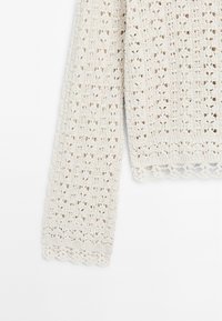 Hellbeige gestrickter Pulloverärmel mit Ausbrennermuster und gewelltem Abschluss. Hergestellt aus strukturiertem Garn, das das atmungsaktive Design betont.