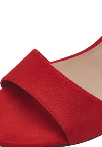 Sandalia de ante rojo con una tira ancha en la parte superior y una suela beige suave, con un diseño minimalista y sin hardware visible.