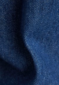 Denim stof in diepblauw met een gestructureerde weving en een lichte glans, toont opvallende stiksels en heeft een zachte, flexibele val.