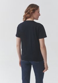 T-shirt en coton noir avec un col rond classique, des manches courtes et un ourlet droit ; porté avec un jean en denim bleu.