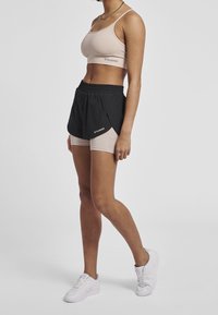 Beige sportbh och svarta shorts med ljusa accentfärger. Shorts har resårmidja och en lagerdesign. Vita sneakers fulländar looken.