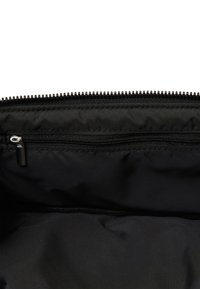 Interno della borsa in tessuto nero che mostra una tasca orizzontale con cerniera e il bordo superiore di una chiusura con cerniera metallica.