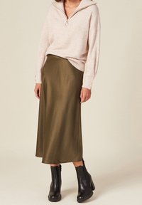 Maglione zip-up rosa chiaro con una vestibilità rilassata, abbinato a una gonna midi in satin verde oliva e stivaletti neri con tacco largo.