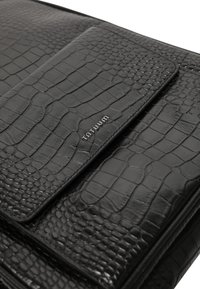 Czarna torba ze skóry tłoczonej wzorem krokodyla o gładkiej fakturze, wyposażona w klapę zamknięcia i srebrny detal z logo "Tontuum".