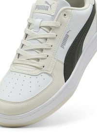 Zapatilla de cuero blanca con detalles en negro, panel lateral texturizado, puntera perforada y cordones planos. Presenta el logo de Puma en la lengüeta y en el lateral.