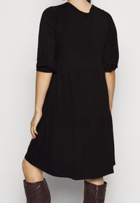 Svart knälång klänning med rund halsringning, puffärmar och lager-på-lager kjol. Tillverkad av mjukt tyg, med en lös passform.