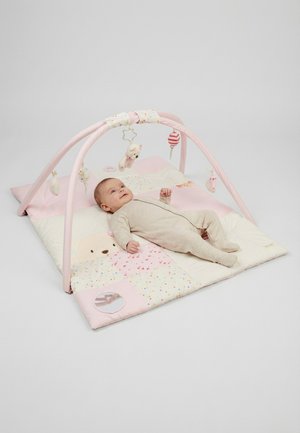 Baby in beige onesie lying on pink and white play mat with soft toy arches and hanging plush toys.