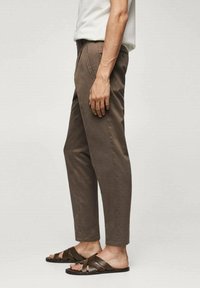 Pantalon chino marron coupe slim, avec poches latérales et texture subtile. Associé à des sandales à lanières marron foncé.