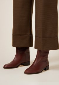 Bruine leren enkellaarsjes met een ronde neus en een gestapelde blokhak, gedragen met bruin geruit broek met een brede zoom.
