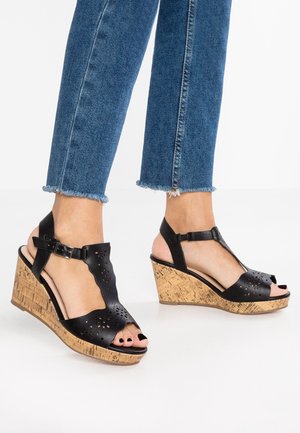 Czarne sandały na klinie z korkową podeszwą, laserowo wycinane detale, odkryte palce i regulowany pasek na kostce. Teksturowana cholewka i gładka wyściółka wewnętrzna.