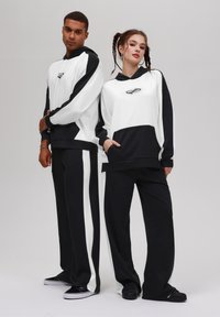 Sweatshirts à capuche noir et blanc avec des motifs géométriques, assortis de pantalons avec un motif coloré. Des chaussures décontractées sont incluses.