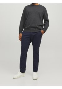 Grå stickad tröja med rund halsringning, bärs tillsammans med marinblå chinos. Vita sneakers kompletterar outfiten och visar upp en avslappnad stil.