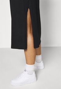 Czarna midi sukienka z bocznym rozcięciem, w parze z białymi sneakersami i białymi skarpetkami do kostek. Gładki materiał, casualowy krój i luźny fason.