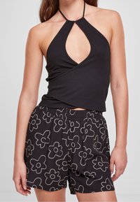Czarny top na halterneck z dekoltem w kształcie dziurki w parze z czarnymi szortami z białym kwiatowym wzorem i elastycznym paskiem w talii.