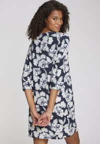 Abito floreale navy con maniche a tre quarti, vestibilità comoda e una grande stampa di fiori bianchi con foglie verdi. Tessuto dalla texture liscia.