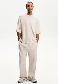 Beige oversized t-shirt with short sleeves, paired with light beige wide-leg trousers. Features smooth fabric and minimalistic design accents.