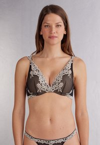 Černá krajková podprsenka s trojúhelníkovým tvarem a krémovými květinovými krajkovými detaily kolem okrajů a ramínek, což dodává texturovaný efekt.