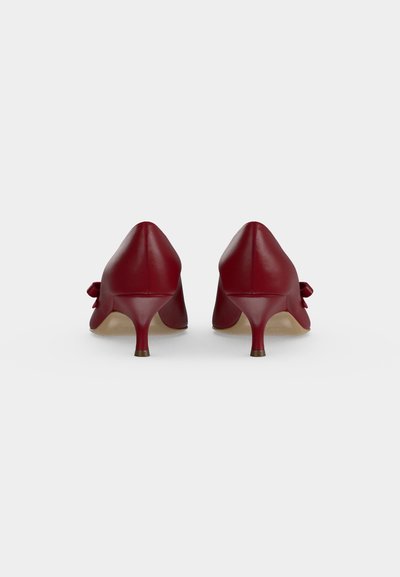 Paire de chaussures basses en cuir rouge avec un détail nœud sur les côtés, vues de dos sur un fond blanc uni.