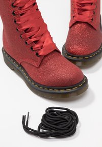 Röda glittriga ankelskor med sidenremmar, rund tå, svart sula med gula sömmar, kompletterade med svarta skosnören.