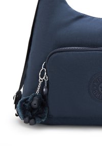 Marinblå tygaxelväska med en dragkedjeförsedd framficka, har en fluffig charm i form av en gorilla och en cirkulär logodetalj.