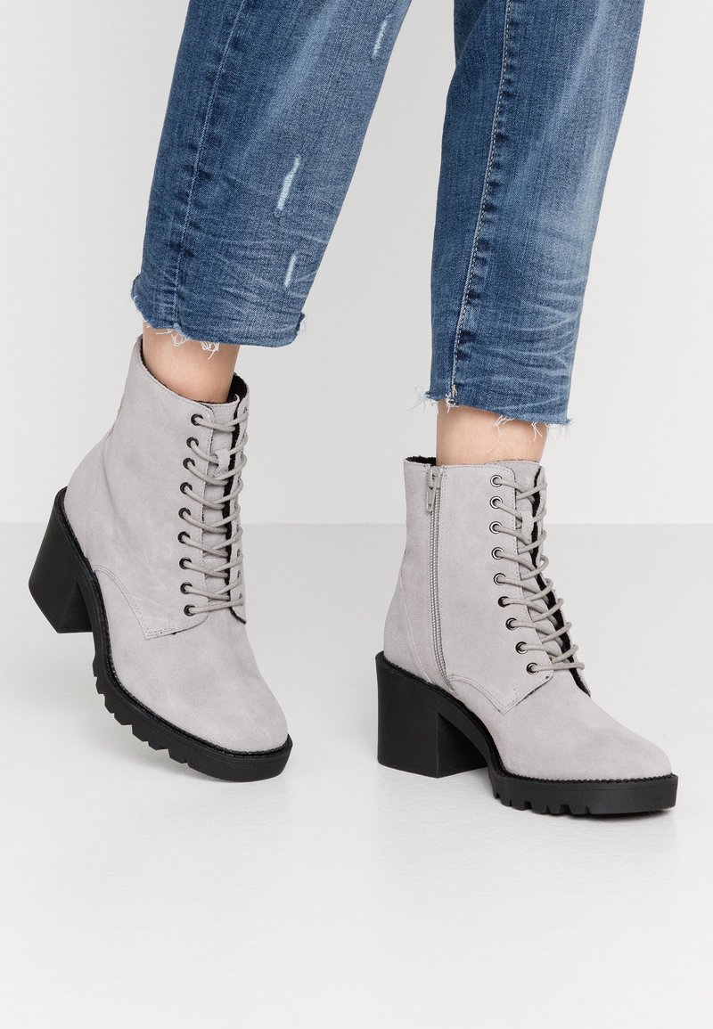 Botas de tobillo de ante gris con cordones en la parte delantera, cremallera lateral, tacón cuadrado y suela de goma texturizada. Llevadas con jeans azules recortados.
