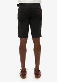 Pantaloni short neri in cotone con vita foderata, tasche posteriori e orlo arrotolato. Indossati con scarpe bordeaux con dettagli a lacci.