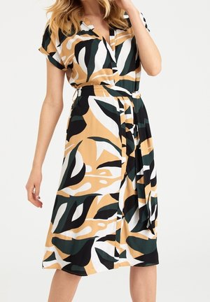 Robe multicolore avec un design croisé, un décolleté en V, des manches courtes et une taille nouée. Le tissu présente des motifs de feuilles abstraites vertes et noires sur un fond beige.