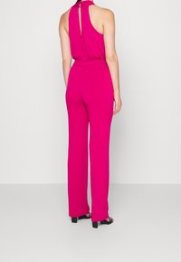 Fuchsia jumpsuit met een halternek en een keyhole rugontwerp. Heeft een aansluitend lijfje en wijde pijpen. Gladde textuur, geen zichtbare patronen.