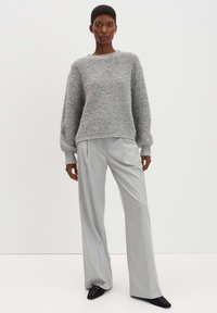 Maglione grigio a maglia con finitura testurizzata, abbinato a pantaloni larghi grigi chiaro. Scarpe slip-on nere con decorazioni.