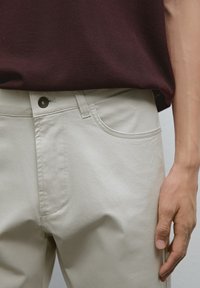 Beiga bomullbyxor med en framficka, knappstängning och subtila sömnadsdetaljer, kombinerade med en mörk maroon stickad topp.