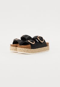 Schwarze Plateausandalen mit zwei breiten Riemen, goldenen runden Beschlägen und einer aus Naturseil gewickelten Sohle. Flacher Fußbett für Komfort.