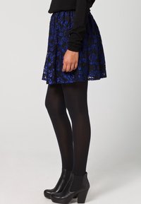 Gonna in pizzo nero con motivi floreali blu, vita elasticizzata e forma svasata. Abbinata a calze nere aderenti e stivaletti con tacco largo.