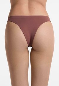 Bruine bikinionderbroek met een gladde textuur, minimalistisch ontwerp en een dunne tailleband, zichtbaar van achteren.