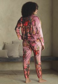 Zestaw do noszenia w domu z nadrukiem kwiatowym z różowego satynu, charakteryzujący się luźnym krojem, długimi rękawami, elastycznymi mankietami oraz pasującymi spodniami dresowymi z elastycznym ściągaczem przy kostkach.