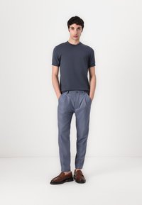Šedé tričko s krátkým rukávem v kombinaci se světle modrými plisovanými kalhotami. Hnědé mokasíny dotvářejí outfit. Jednoduchý, moderní design.