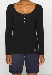 Zwarte geribbelde lang- mouw t-shirt met een ronde hals, decoratieve knopen en een witte geborduurde logo. Draag het met navy korte broek.