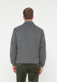 Giacca grigia in misto lana con colletto strutturato, maniche lunghe e polsini a costine. Presenta un design posteriore pulito e minimale.