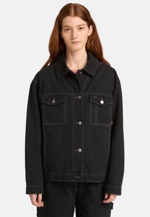 Zwarte denimjas met een puntige kraag, knoopsluiting aan de voorkant, twee borstzakken, contrasterende stiksels en een losse pasvorm.