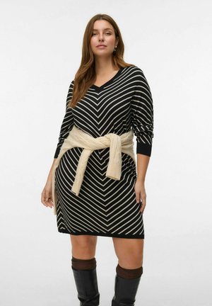 Zwart-wit gestreepte gebreide jurk met een V-hals en lange mouwen, voorzien van een beige gebreide riem geknoopt in de taille. Zwarte knie-hoge laarzen.