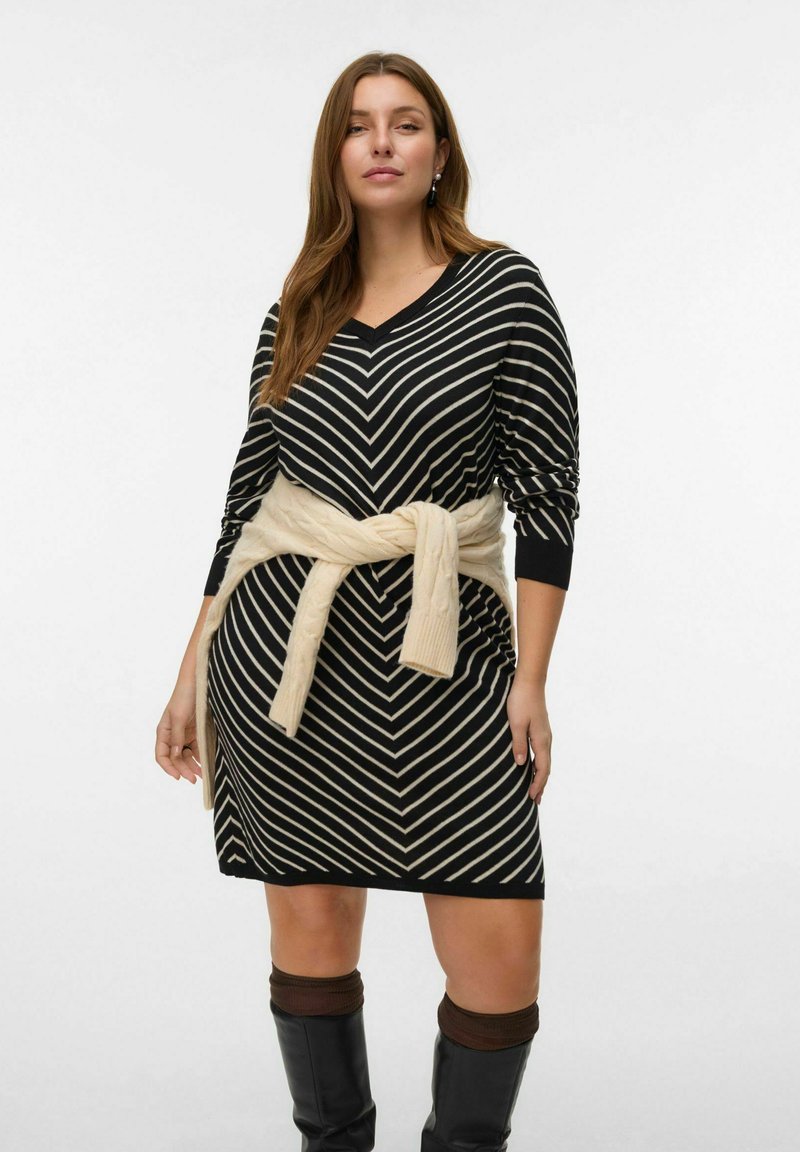 Robe en tricot noir et blanc à rayures avec un col en V et des manches longues, dotée d'une ceinture en tricot beige nouée à la taille. Bottes noires montantes.