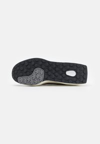 Sole di scarpe in gomma nera con grip texture, caratterizzata da un accento grigio vicino al tallone e motivi circolari per la trazione. Profilo piatto, senza segni di usura visibili.