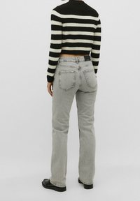 Jersey recortado a rayas en blanco y negro, con cuello alto; vaqueros rectos grises con dos bolsillos traseros; zapatos negros.