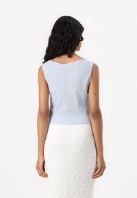 Top sem mangas em azul claro, com decote em bico. Textura macia e design cropped, apresentando bordas levemente recortadas.