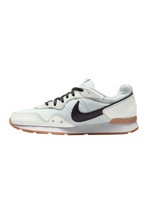 Biało-beżowy sneaker Nike z czarnym logo słynnego znaku, czarnymi sznurówkami i jasno brązową podeszwą, pokazany z boku na białym tle.