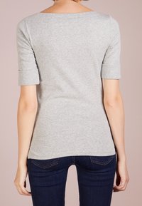 Šedý top s krátkým rukávem a širokým výstřihem, přiléhavý střih a ohrnuté rukávy. Vyrobeno z měkké, hladké látky s uniformní texturou.