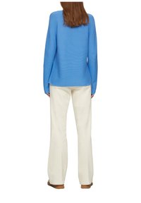 Ljusblå stickad tröja med lång ärm, ribbad struktur och rundad fåll, kombinerad med krämfärgade utsvängda byxor.